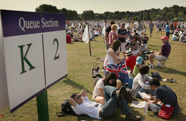 Tennis fans queue in the early morning sunshine for the Wimbledon Tennis Championships 