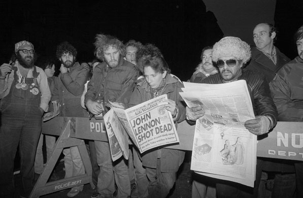 Crowds gather outside John Lennon's apartment reading newspapers reporting his death