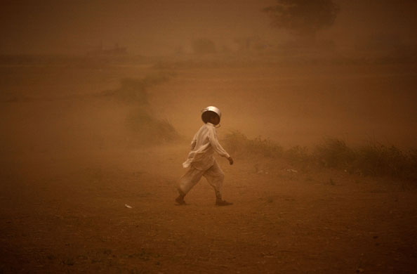 24 hours in pictures: A displaced boy covers his head with a cooking pot during a sand storm