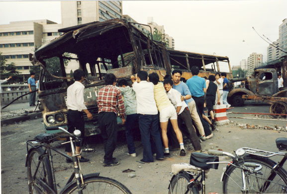 Tiananmen protests 1989: After the tank patrol passes, civilians push buses back at a roadblock