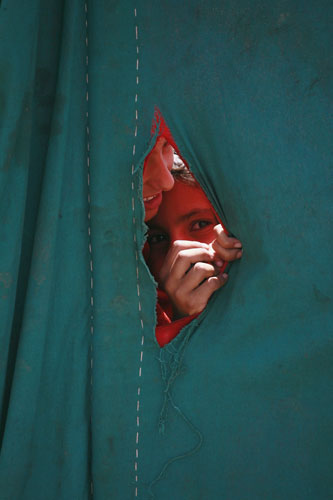 24 hours in pictures: An internally displaced girl looks through a tear in a tent at UNHCR camp