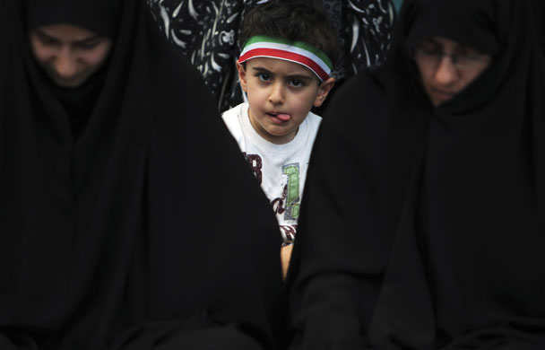 Iran elections: A boy wearing a headband peers behind women attending Friday prayers 