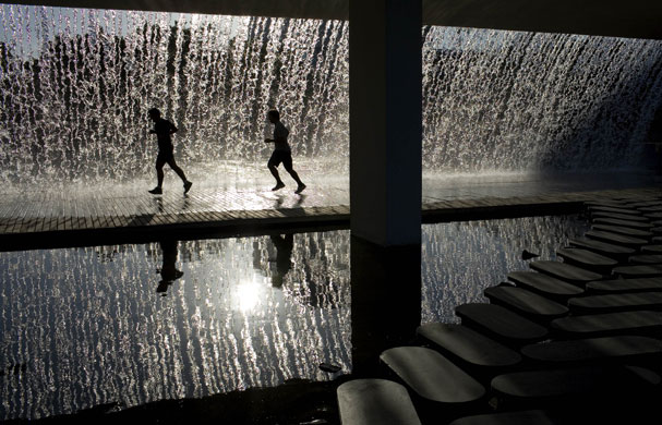 16 July 2009: Lisbon, Portugal: Joggers run under a fountain