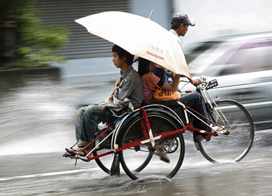26 July 2009: Yangon, Myanmar: A man on a tricycle transports residents after a downpour