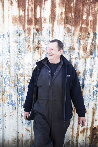 Manchester East 1 - 10: A man stands smiling in front of a corrugated iron fence