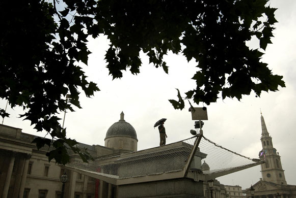 weather london: Person stands in rain on the Fourth Plinth in Trafalgar Square