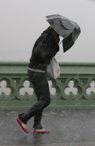 weather london: A woman struggles through wind and rain in London