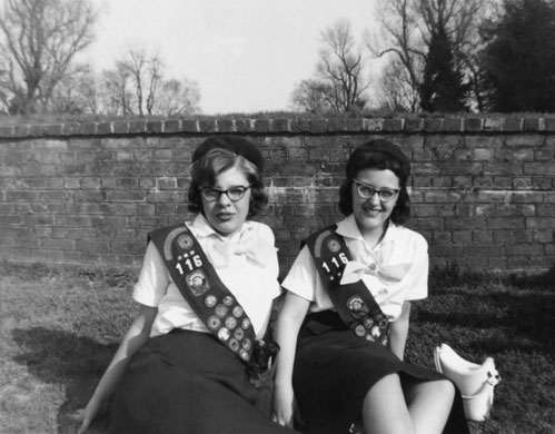 Girl guides 100th: 1959: Girl scouts sitting on the grass by brick wall