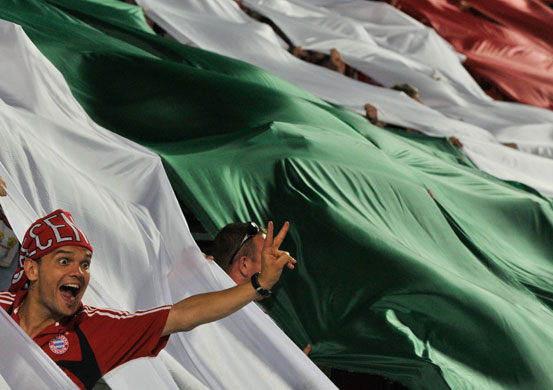 champions league: A happy Debreceni VSC fan gestures from behind a giant Hungarian flag