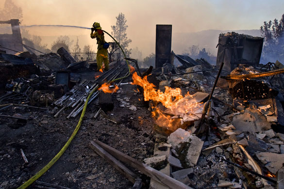 California wildfires: A firefighter spraying water on hot spots of a house