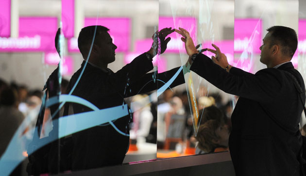 Week in Business: A fairgoer flips a picture on the stand of Deutsche Telekom