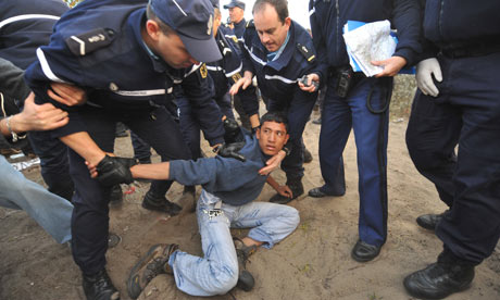 French police detain a migrant at a camp called the jungle near Calais