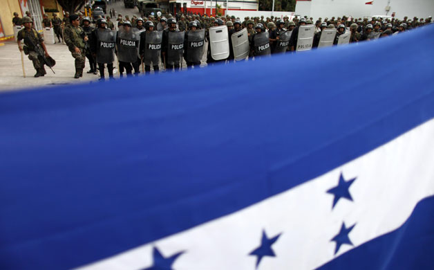 Honduras crisis: Soldiers stand guard as supporters of Zelaya hold a flag 
