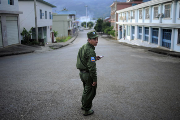 4 September 2009: Namteuk, Myanmar: A policeman uses his mobile phone as he patrols a street