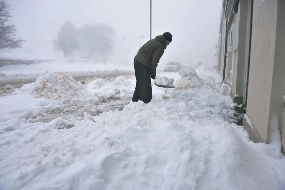 Snowing again: A man clears snow in Princetown, Dartmoor, Devon