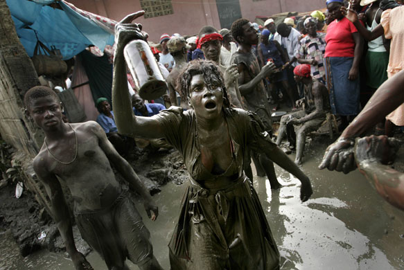 History of Haiti: 2006: A Voodoo believer covered in mud  carries a botle of rum 