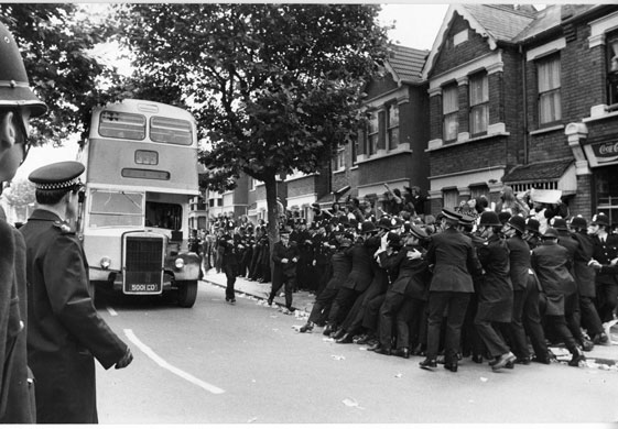Jayaben Desai: A workers bus passes a group of strikers held back by police