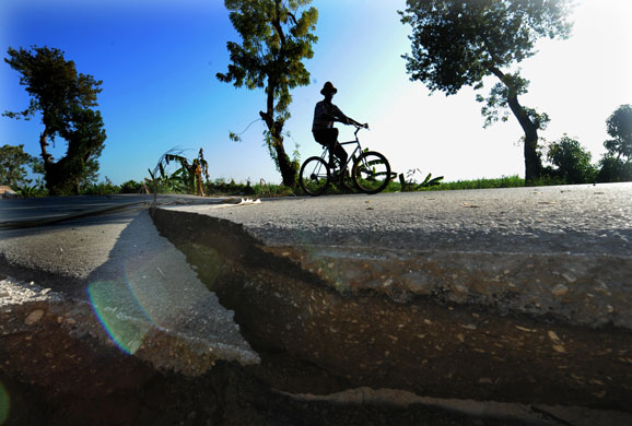 haiti aftermath: A Haitian earthquake survivor peddles past a shattered road in Leogane