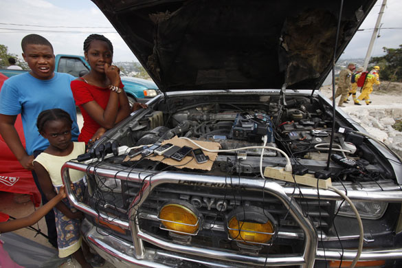 haiti aftermath: Haitians charge mobile phones from a car battery in Port-au-Prince