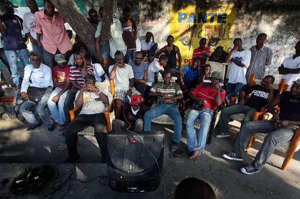 Camps in Haiti: People watch a football match on a television set powered by a generator