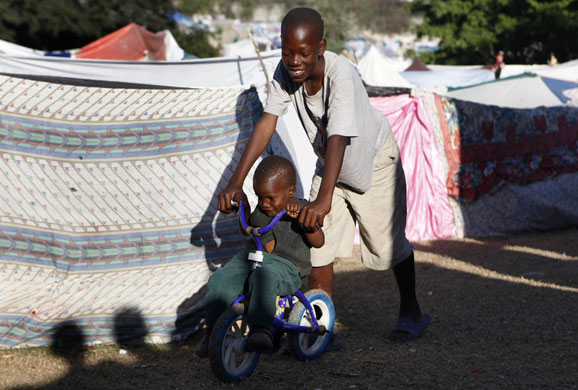 Camps in Haiti: A boy pushes a child on a bike inside a makeshift camp in Port-au-Prince