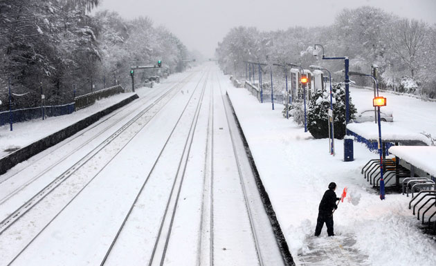Winter weather: A woman tries to remove snow from a platform at a train station in Fleet