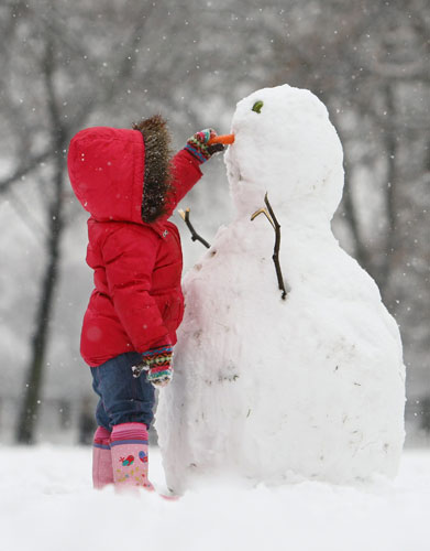 Winter weather: London:  A young girl makes a snowman at Highbury Fields 