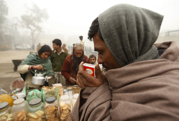 Northern hemisphere: New Delhi, India: A man lights tobacco at a tea stall