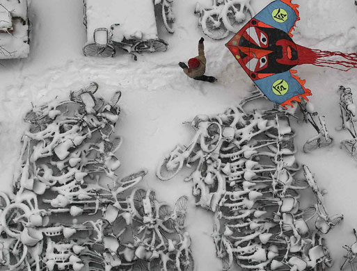 Northern hemisphere: Beijing, China: A child flies a kite over snow-covered bicycles 