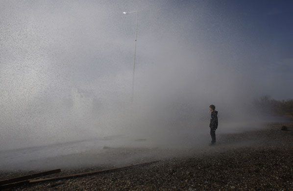 24 hours in pictures: Flisvos, Greece: A boy looks on as a wave crashes into a coastal barrier