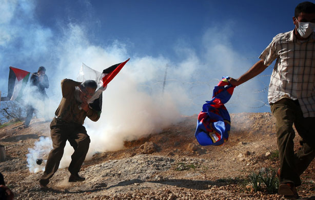 24 Hours in Pictures: A Palestinian uses a plastic bag to protect himself from tear gas