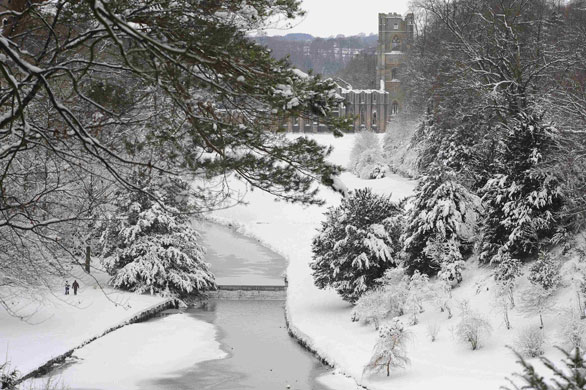 Snow: A couple walk near Fountains Abbey with its snow covered grounds in Ripon