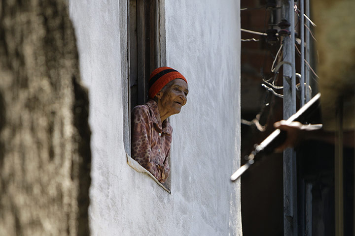 24hours:  A woman looks from her window as police officers patrol, Rio de Janeiro