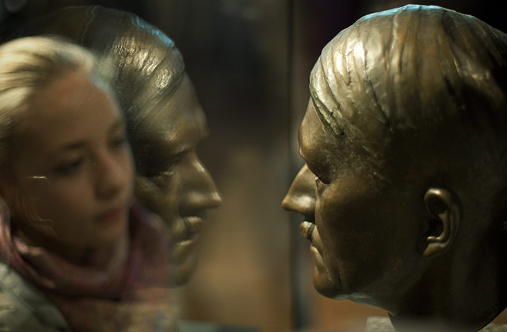24 Hours in Pictures: A visitor stands behind the reflection of a bust of Adolf Hitler