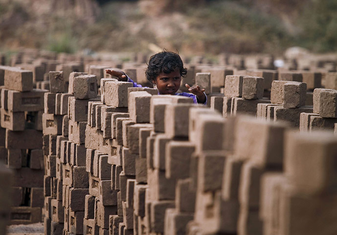 24 hours: Islamabad, Pakistan: A girl plays with bricks next to her mother at a kiln