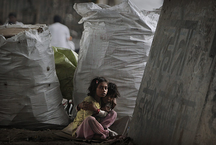 24 Hours in Pictures: Homeless Indian girls sit under an overpass by bags of recyclable material