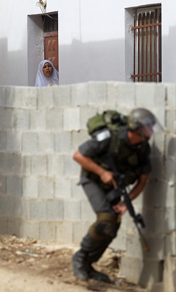 24 Hours in Pictures: A Palestinian woman looks out from her house at an Israeli border policeman