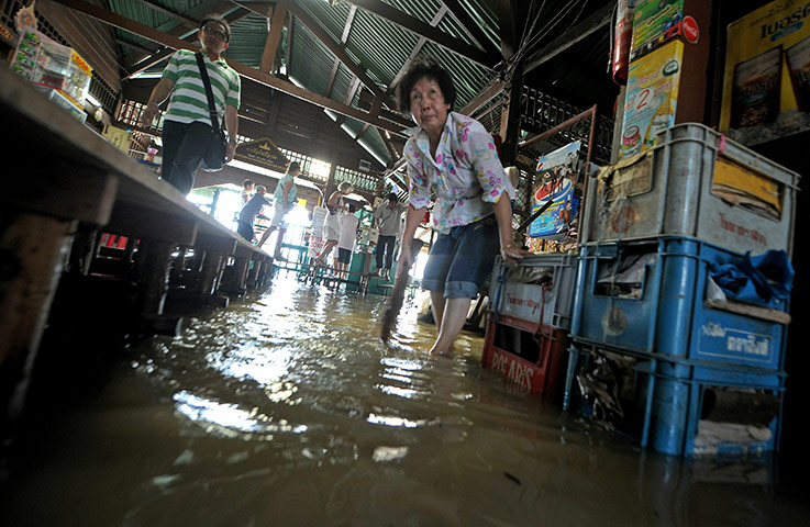 24 Hours In Pictures: A Thai woman cleans the floor of a flooded market in Bangkok