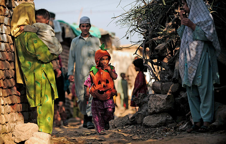 24 hours in pics: A Pakistani girl wearing a halloween costume walks through a slum area