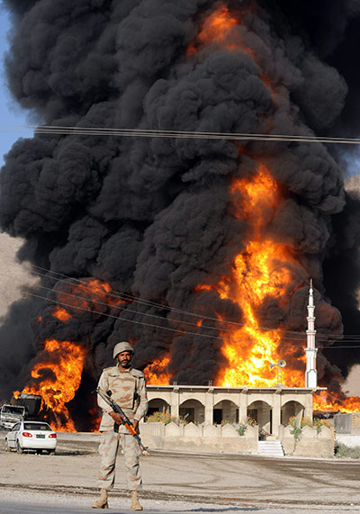 Pakistan tankers attack: A Pakistani paramilitary soldier stands guard in front of burning tankers 