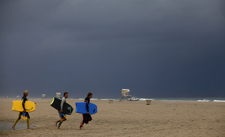 24hours: Surfers carry their boards along the beach as storm clouds darken