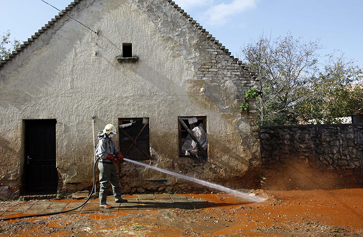 Toxic sludge Hungary: A Hungarian fire fighter cleans a street flooded with toxic mud in Devecse