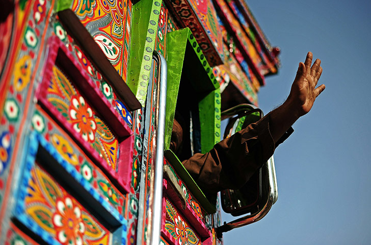 24 hours in pictures: A truck driver waves as he drives the finished painted truck, Pakistan