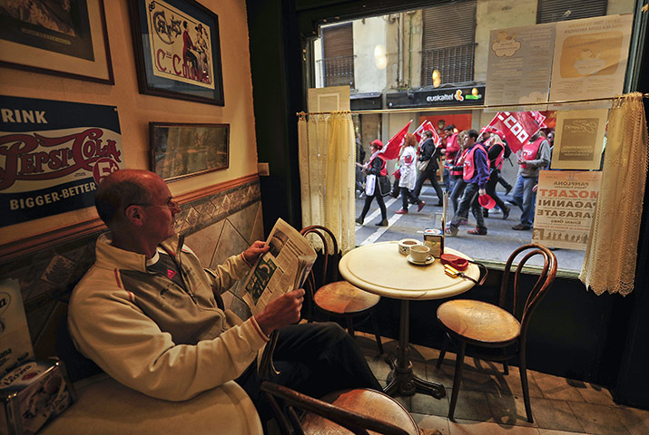 Week in Business: A man reads a paper as strikers pass by during the strike in Pamplona Spain