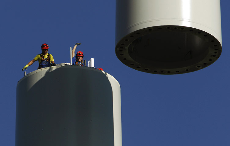 24hours: Workers stand on top of a tube as a crane lifts a part of a  wind turbine