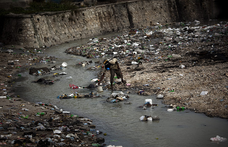 Haiti cholera: A man collects water in a river filled with waste in Port-au-Prince