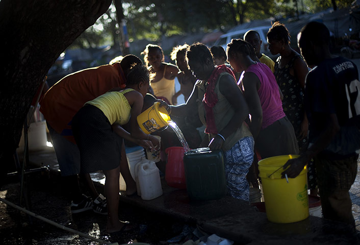 Haiti Cholera Devastation: Women collect water  next to their tents in refugee camp in Port-au-Prince