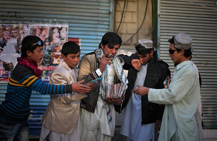 24 hours in pictures: An Afghan vendor smokes a cigarette as Afghan boys purchase pirated CDs