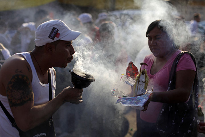 All Saints: A man blows incense smoke at a couple of Santa Muerte