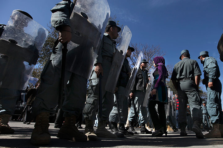 24 hours pics: An Afghan woman protester walks past as policemen stand guard
